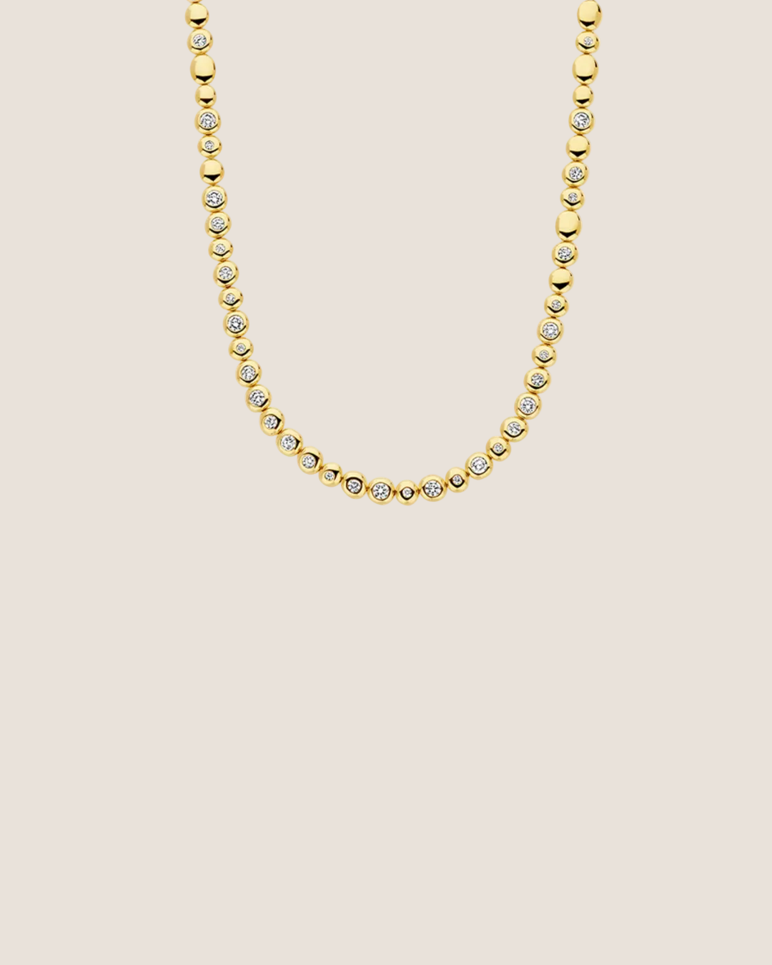 A gold tennis necklace featuring small round bezel-set clear stones, shown against a plain white background.