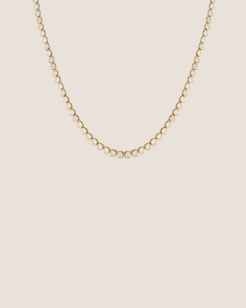 A delicate gold tennis necklace with small clear stones, photographed against a solid white background.