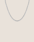 A delicate tennis-style necklace with small clear stones set in a silver-toned metal, shown against a plain white background.