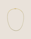 A gold tennis necklace with a small-scale beaded link design, displayed in an oval shape against a solid white background.