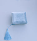 A small light blue velvet square cushion with a matching tassel, photographed against a pale blue background.