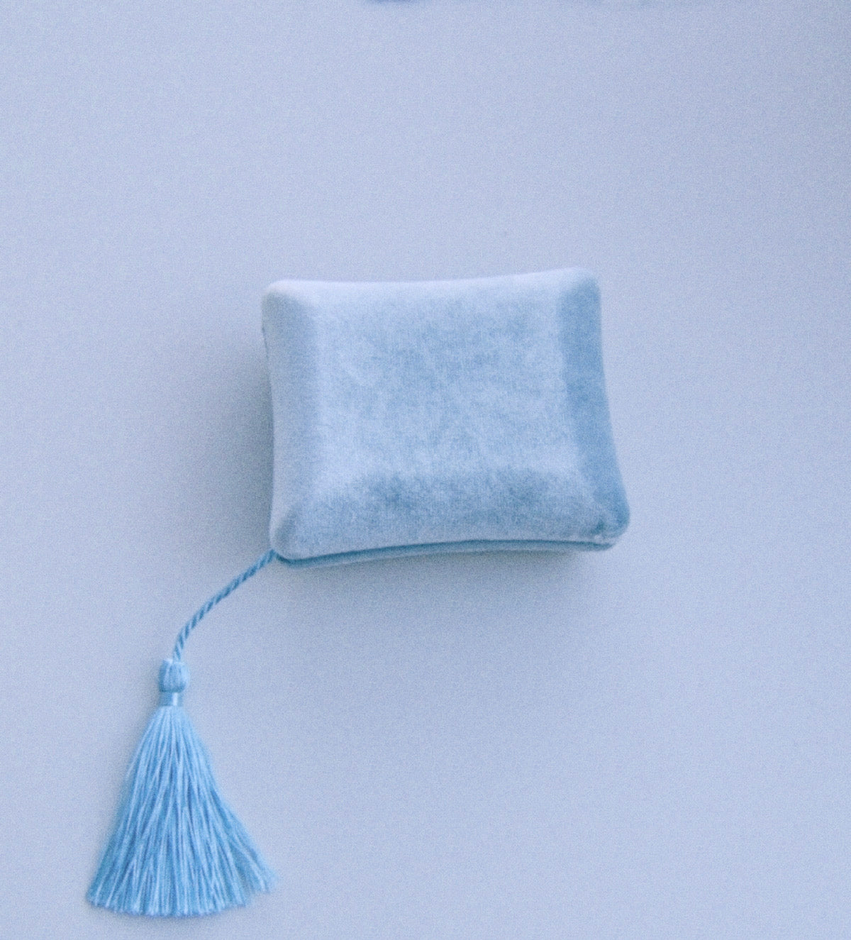 A small light blue velvet square cushion with a matching tassel, photographed against a pale blue background.