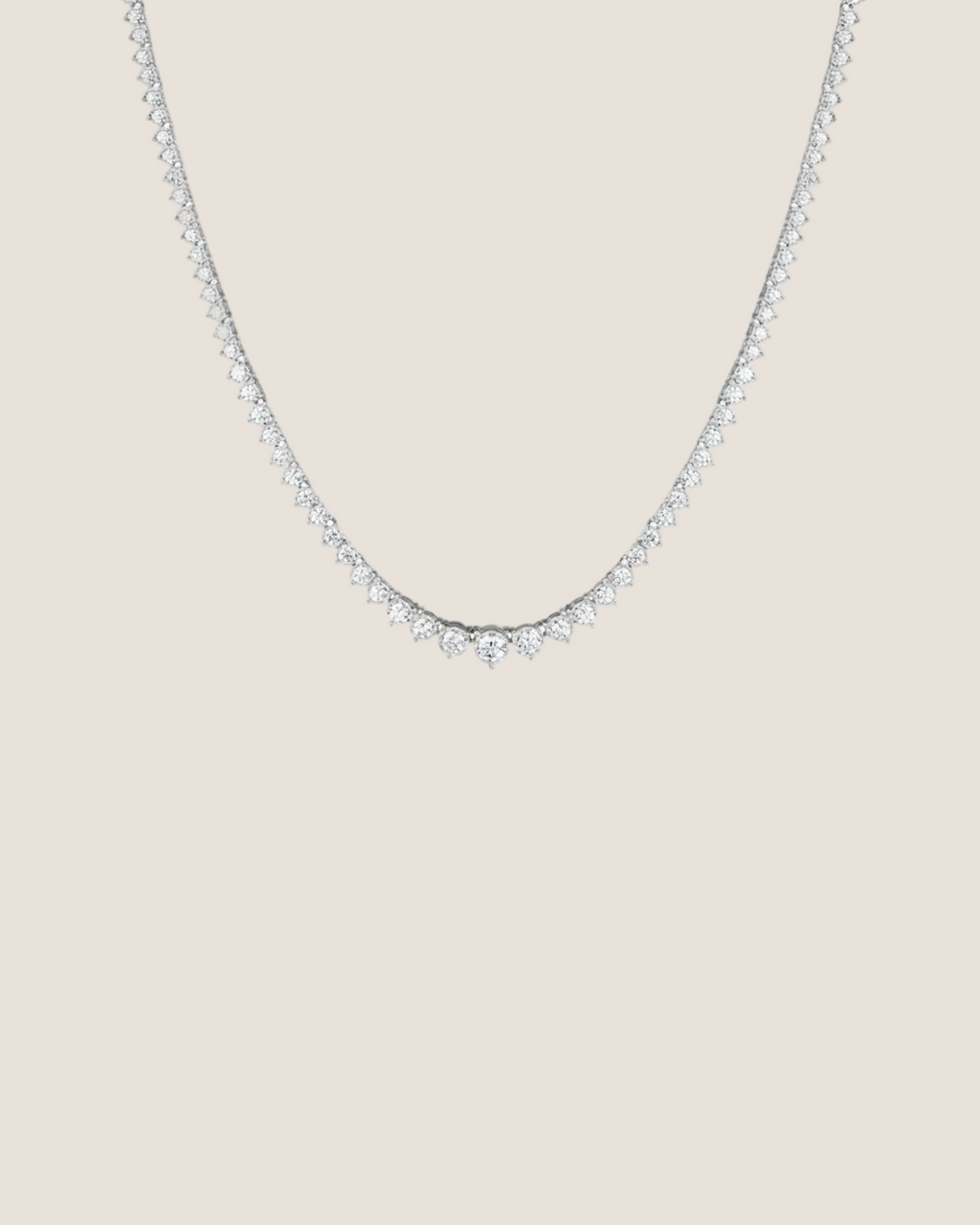 A delicate silver tennis necklace with a row of small clear stones, photographed against a solid white background.