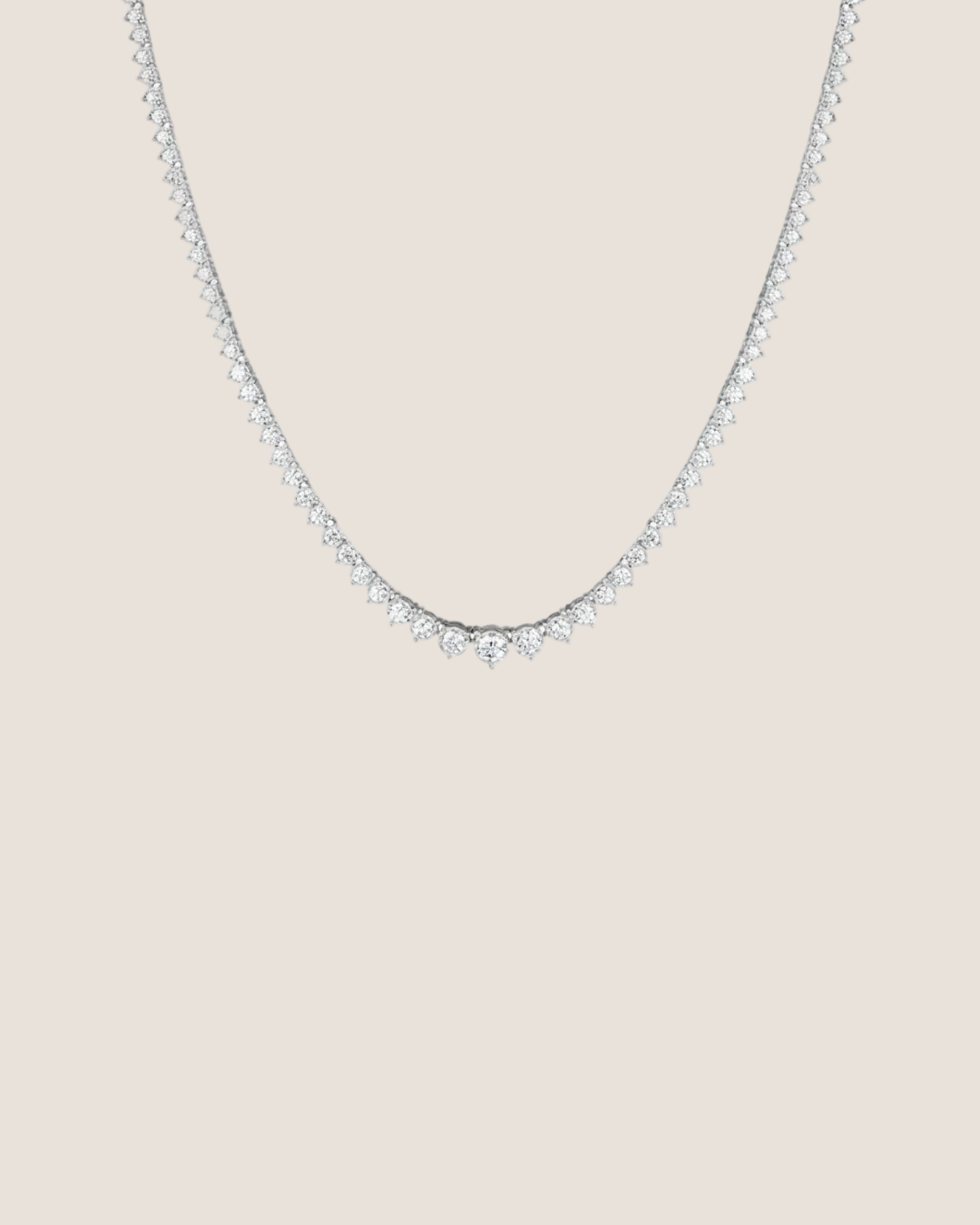 A delicate silver tennis necklace with a row of small clear stones, photographed against a solid white background.